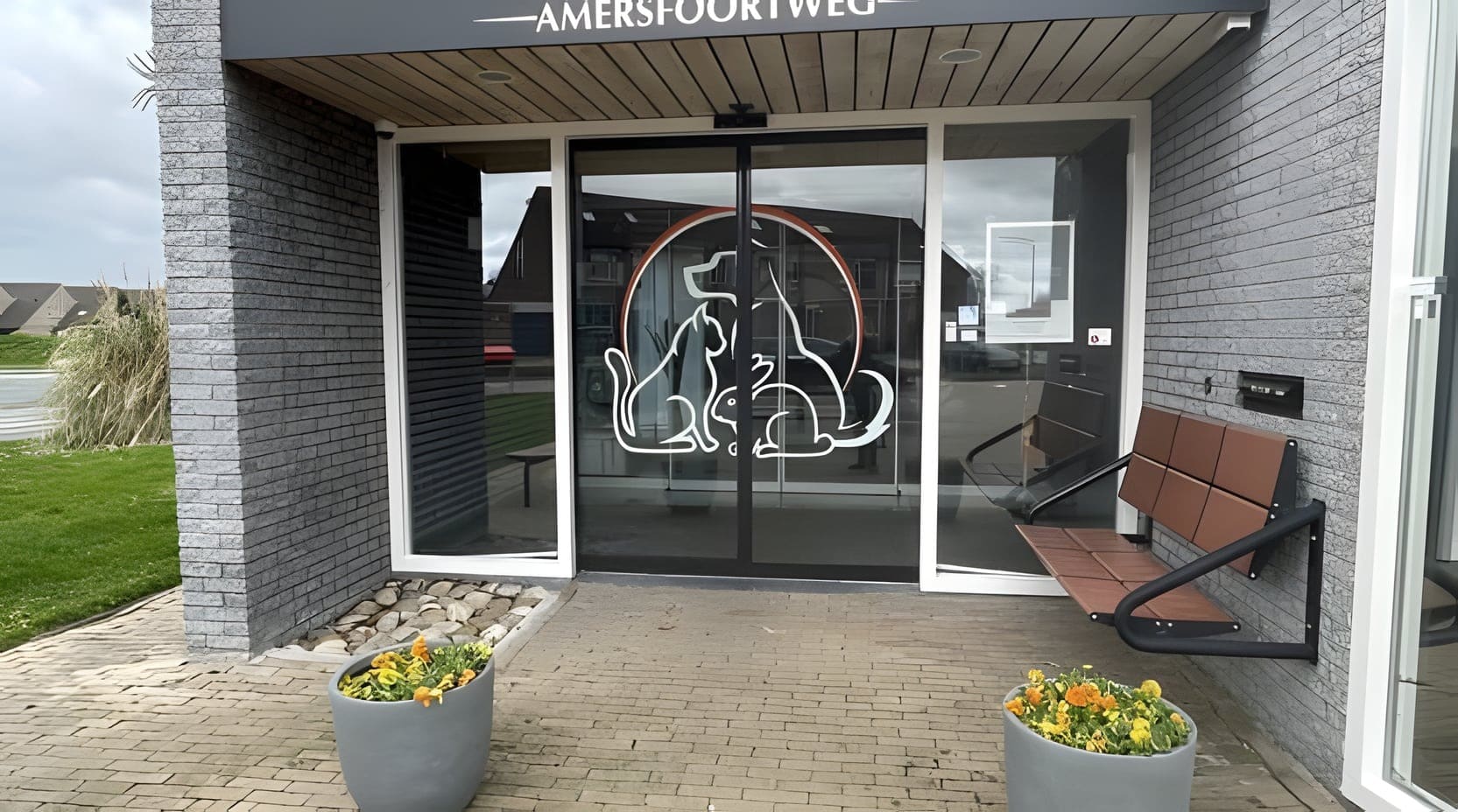 De ingang van Dierenkliniek Amersfoortweg met het logo op de schuifdeur en bloembakken ervoor